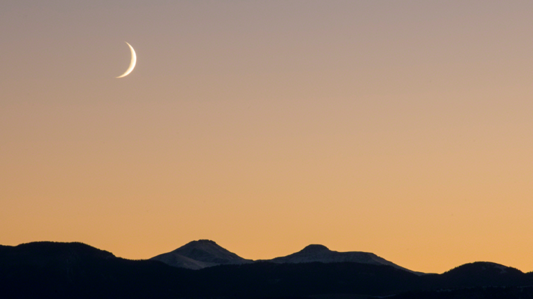 Sky with crescent moon and mountain tops.
