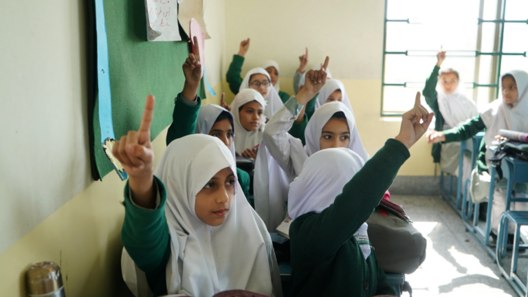 A group of female students raise their hands as they participate in class